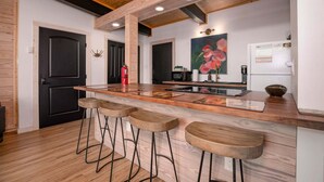 A kitchen with a wooden island, bar stools, a painting, and a refrigerator. - Sunset Ridge (#338) | Walk to Ski Bike Eat! (Basye)