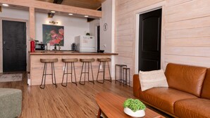 A modern kitchen with wooden bar stools, a dining table with a plant, and a leather sofa. - Sunset Ridge (#338) | Walk to Ski Bike Eat! (Basye)