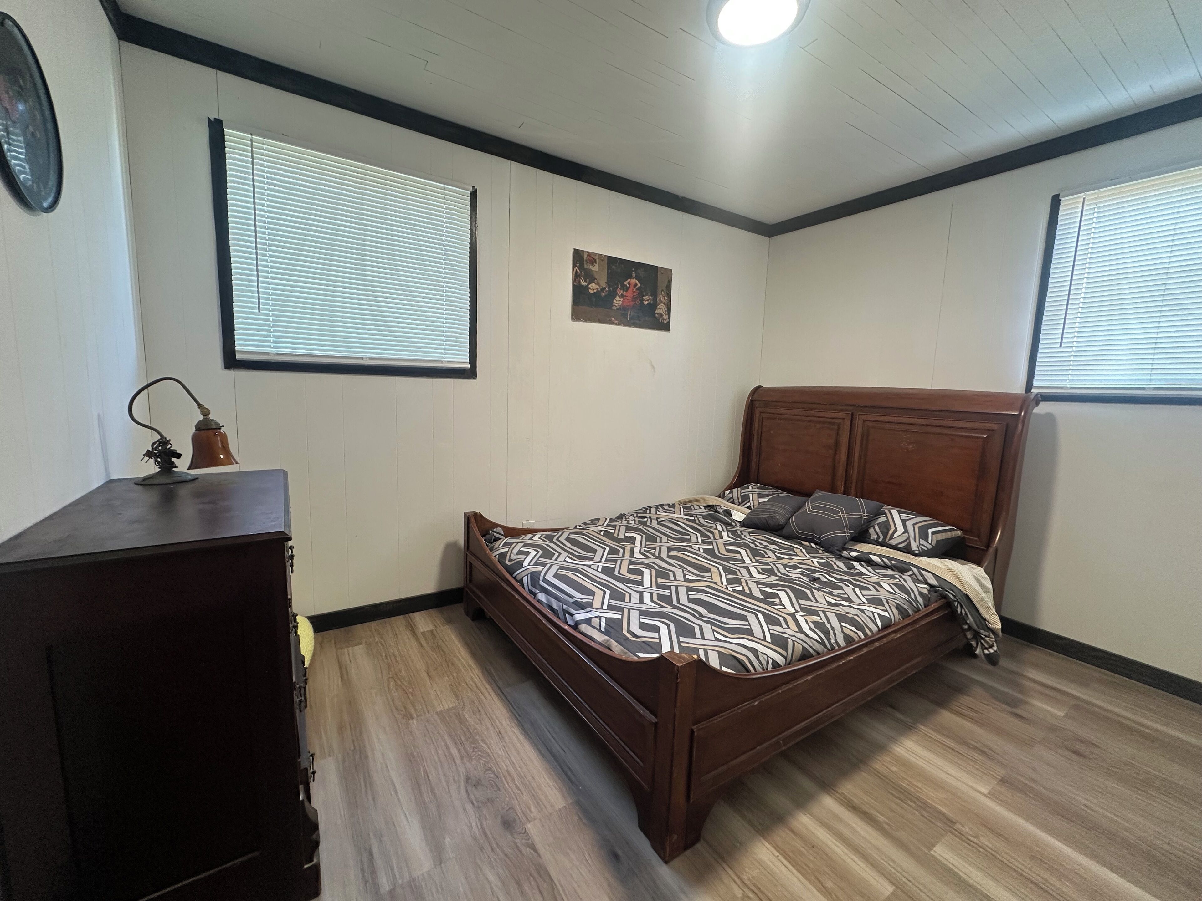 A bedroom with a wooden bed, a dresser, and a wall-mounted lamp.