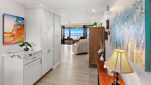 A modern kitchen with white cabinets, a marble countertop, and a view to the living area. - New Listing! Stunning Oceanfront Oasis (Honokowai)