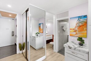 Ein modernes Hotelzimmer mit großem Spiegel, einem Bett, einem Badezimmer mit Dusche und einer Küchenzeile.
