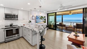 A modern kitchen with a large island, a dining area with a view of the ocean, and a balcony with a view of the sea. - New Listing! Stunning Oceanfront Oasis (Honokowai)