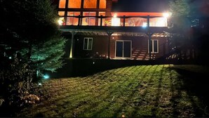 A two-story wooden house with a balcony, illuminated by exterior lights. - Pet Friendly Luxury Cottage (Dysart Et Al)