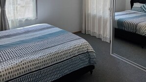 A bedroom with a bed, a large mirror, and an air conditioning unit. - 3BR Airport Stay 10 min to Melbourne Airport (Jacana)