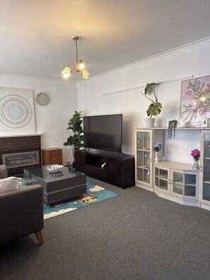 A modern living room with a flat-screen TV, a dark entertainment unit, a sofa, a coffee table, and a decorative rug. - 3BR Airport Stay 10 min to Melbourne Airport (Jacana)
