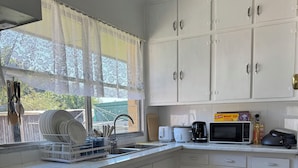 A kitchen with white cabinets, a stove, a sink, and a window with lace curtains. - 3BR Airport Stay 10 min to Melbourne Airport (Jacana)