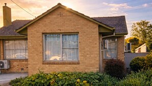 A single-story brick house with a large window, a chimney, and a well-maintained lawn. - 3BR Airport Stay 10 min to Melbourne Airport (Jacana)