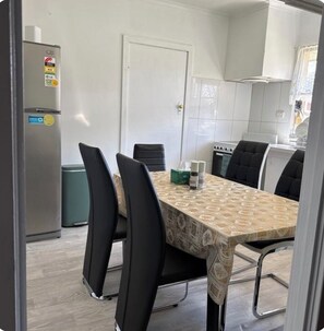 A modern kitchen with a dining table, chairs, and a refrigerator. - 3BR Airport Stay 10 min to Melbourne Airport (Jacana)