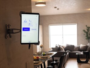 Tabletti, jossa näkyy sisäänkirjautumista varten tarkoitettu käyttöliittymä modernissa hotellihuoneessa, jossa on ruokailutila ja suuri ikkuna.