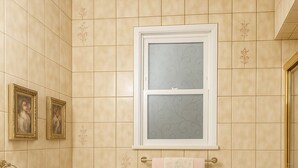 Ein Badezimmer mit beigen Fliesen, einer Toilette, einem Waschbecken, einem Spiegel und gerahmten Bildern an der Wand.