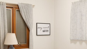 Ein Schlafzimmer mit Holzboden, einem Bett mit blumentückchenmuster-Bettdecke, einem Nachttisch mit Lampe, einem gerahmten Zitat an der Wand und einem Wäschekorb.