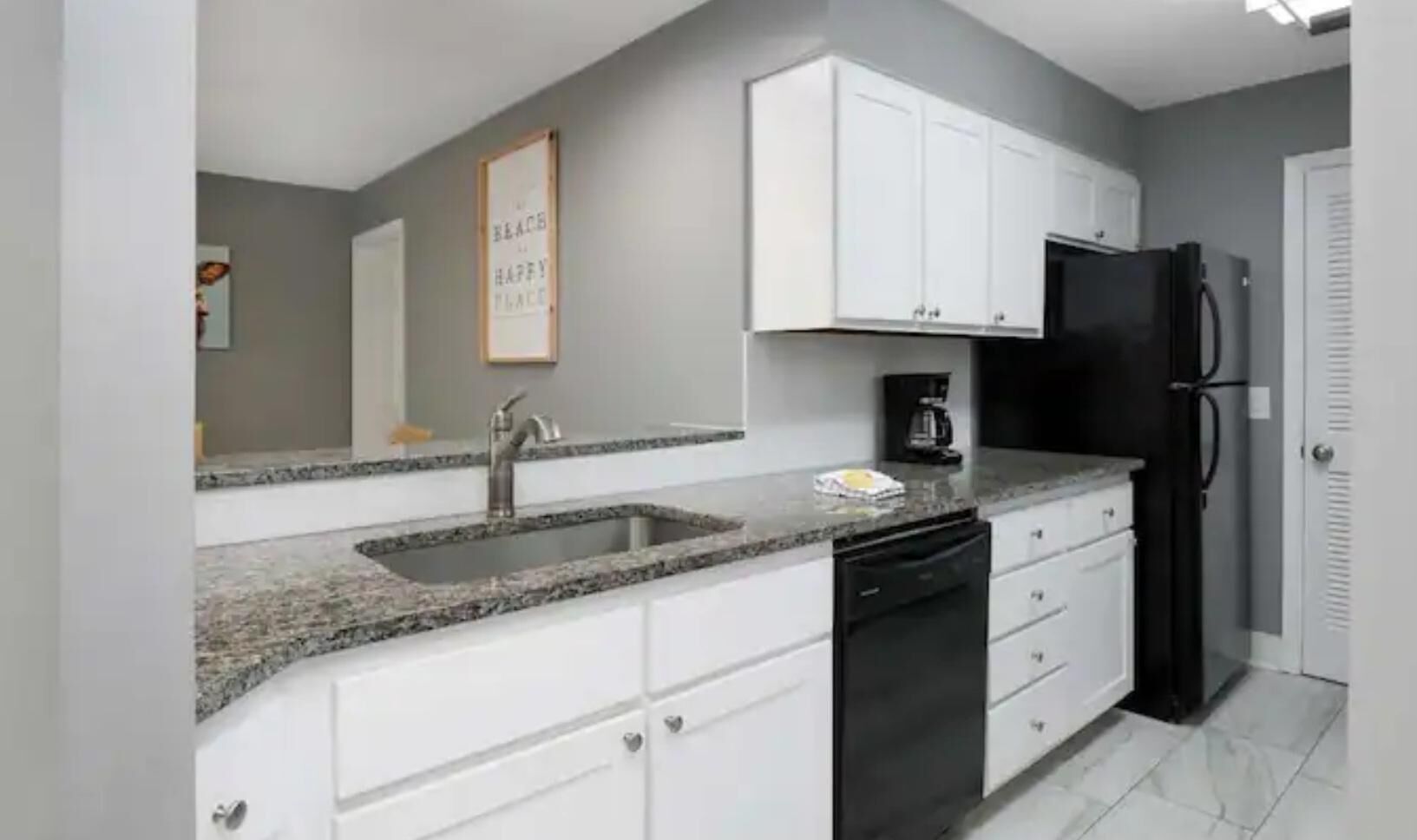 A kitchen with white cabinets, a granite countertop, a black refrigerator, and a dishwasher.