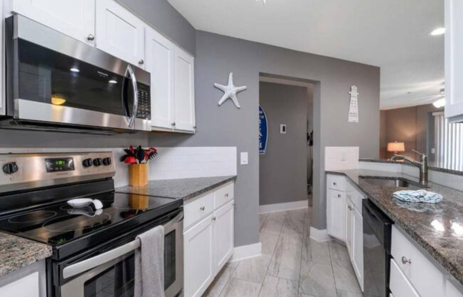 A modern kitchen with stainless steel appliances, white cabinetry, and a granite countertop.