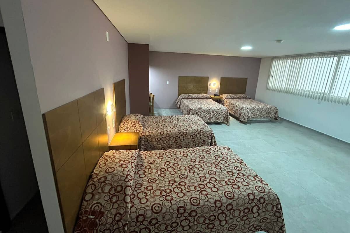 A hotel room with four beds, a small table, and a chair.