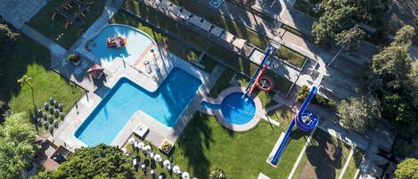 An aerial view of a resort with a large swimming pool, a water slide, and outdoor seating areas.