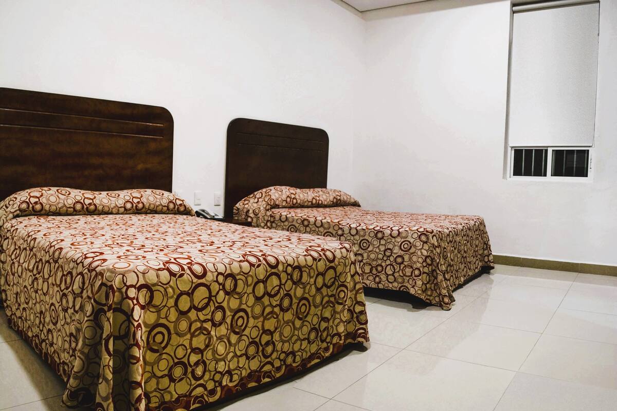 A hotel room with two beds, a wooden headboard, a window with bars, and a tiled floor.