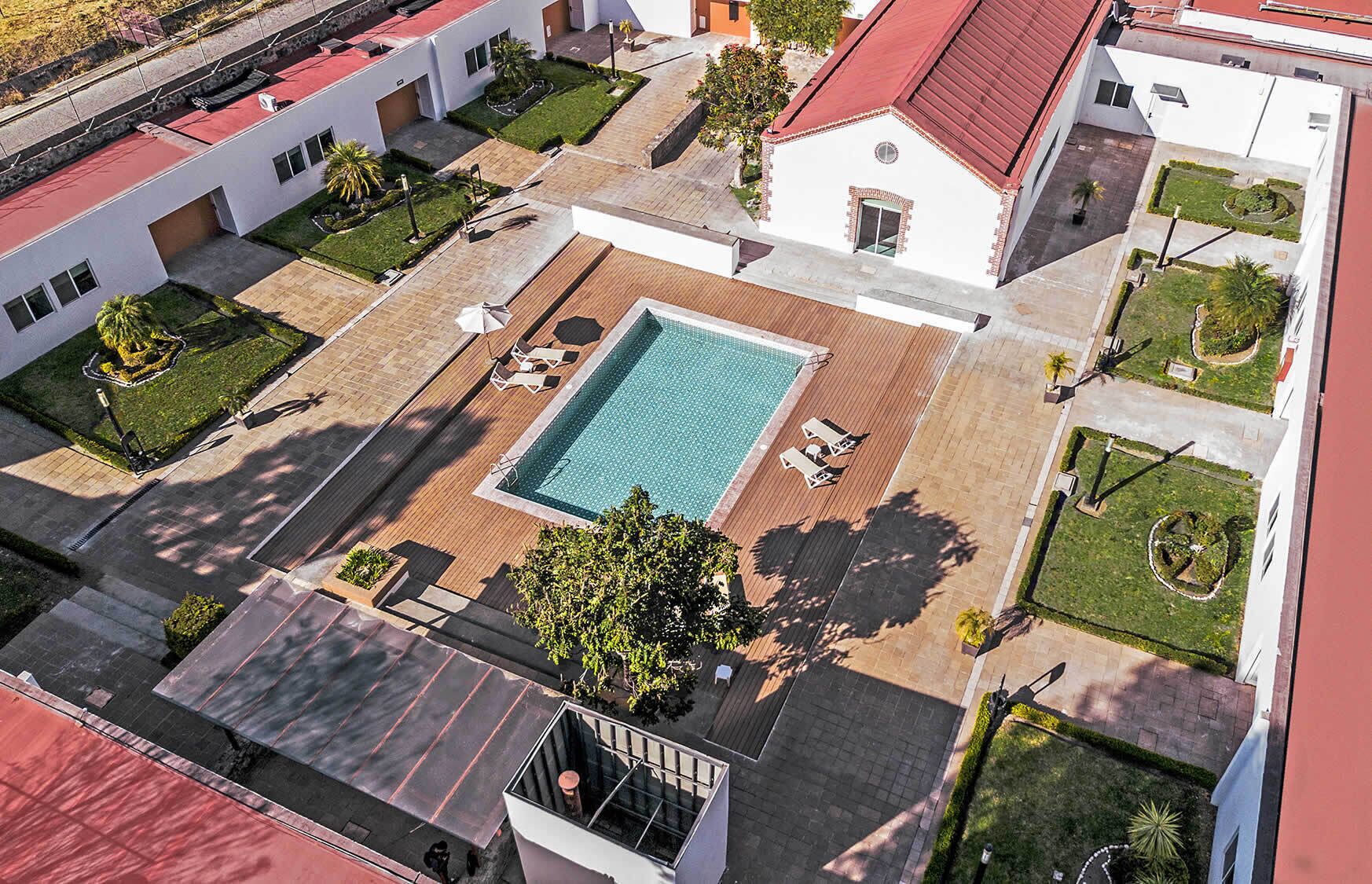 Vista aérea de un hotel con piscina central, varias zonas de descanso y jardines bien cuidados.