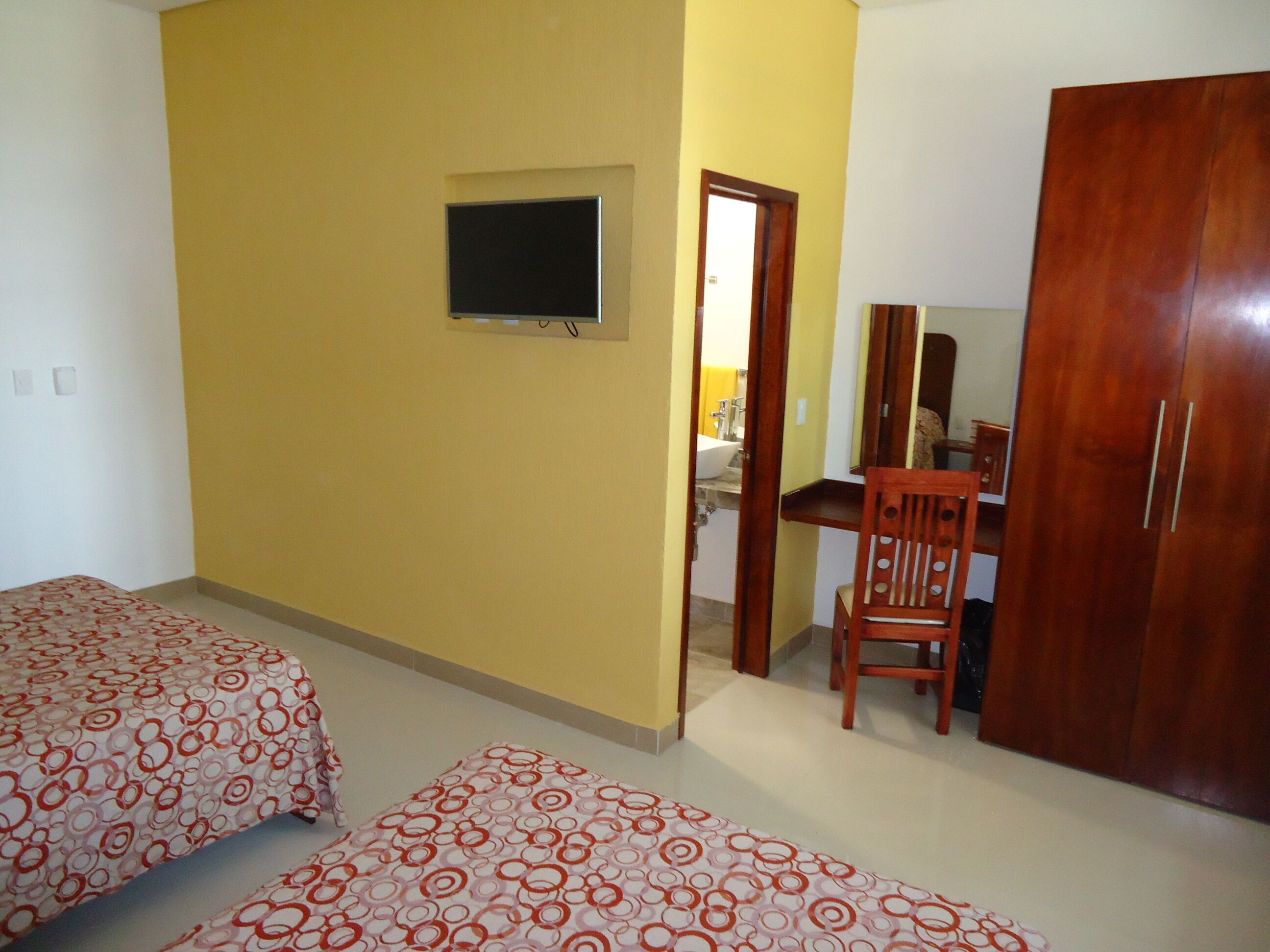A bedroom with two beds, a desk, a chair, a wardrobe, and a television.