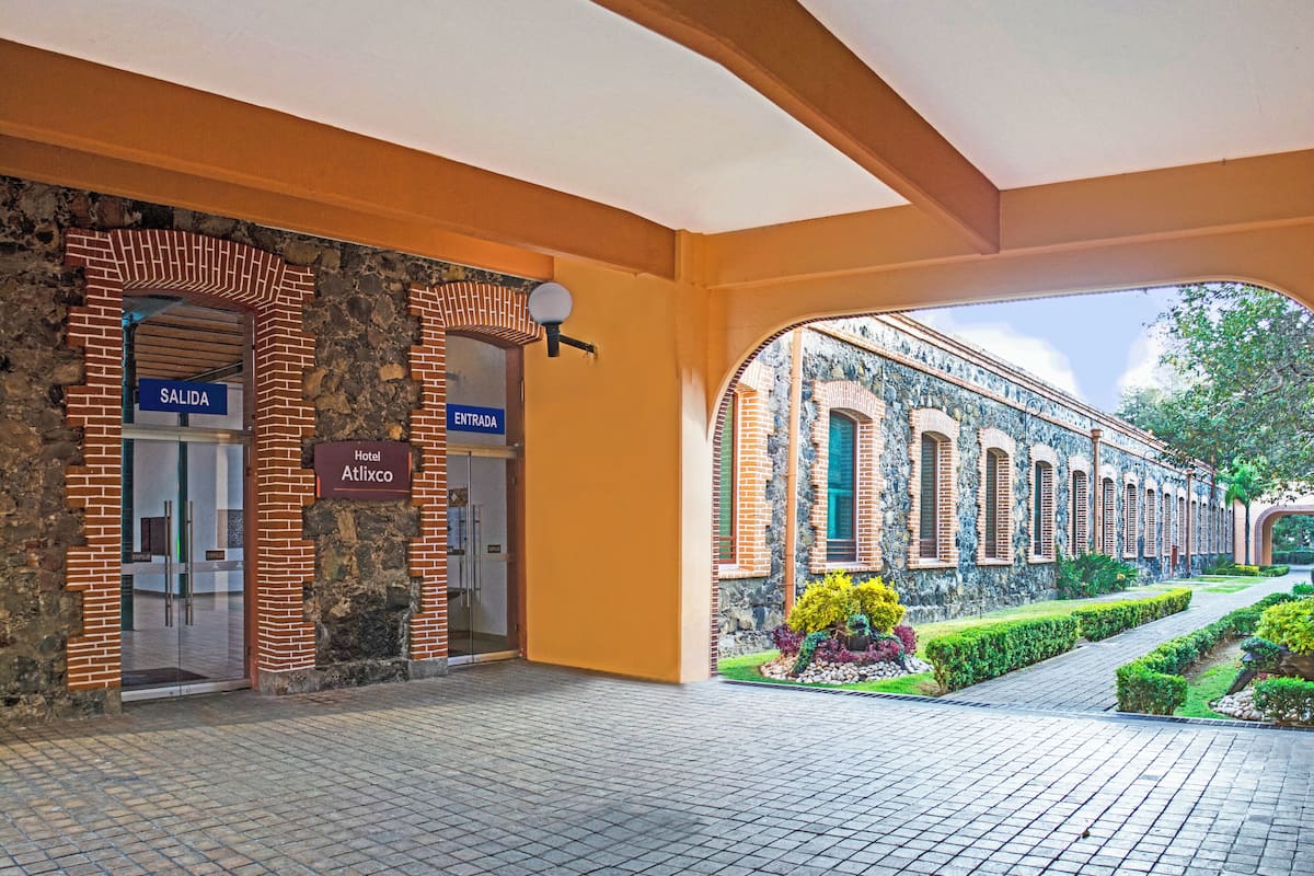 A hotel entrance with a stone facade, a glass door, and a sign indicating 'Hotel Atlixco'.