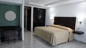 Une chambre d’hôtel moderne équipée d’un lit, d’un bureau, d’une chaise et d’un miroir rond fixé au mur.