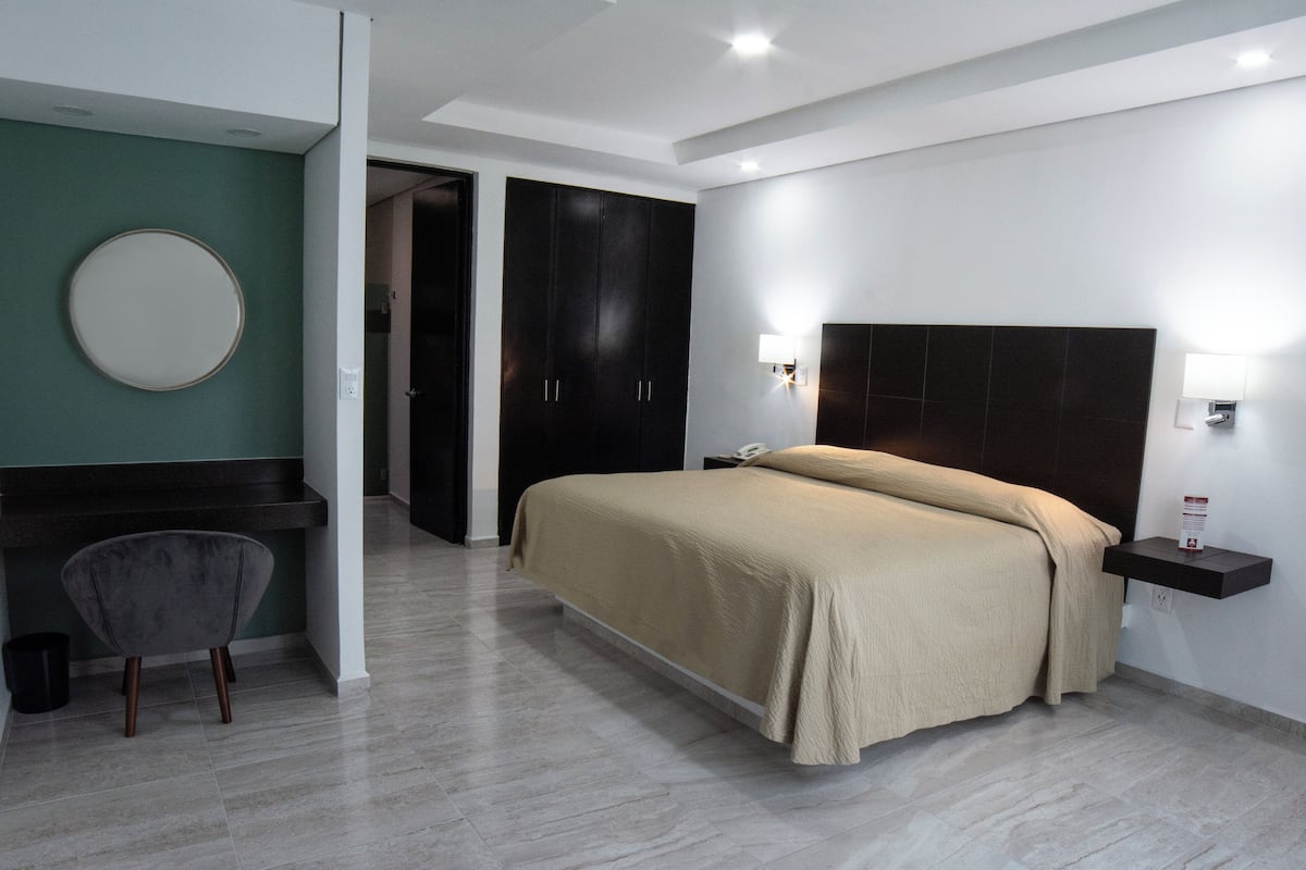 A modern hotel room with a bed, a desk, a chair, and a round mirror on the wall.