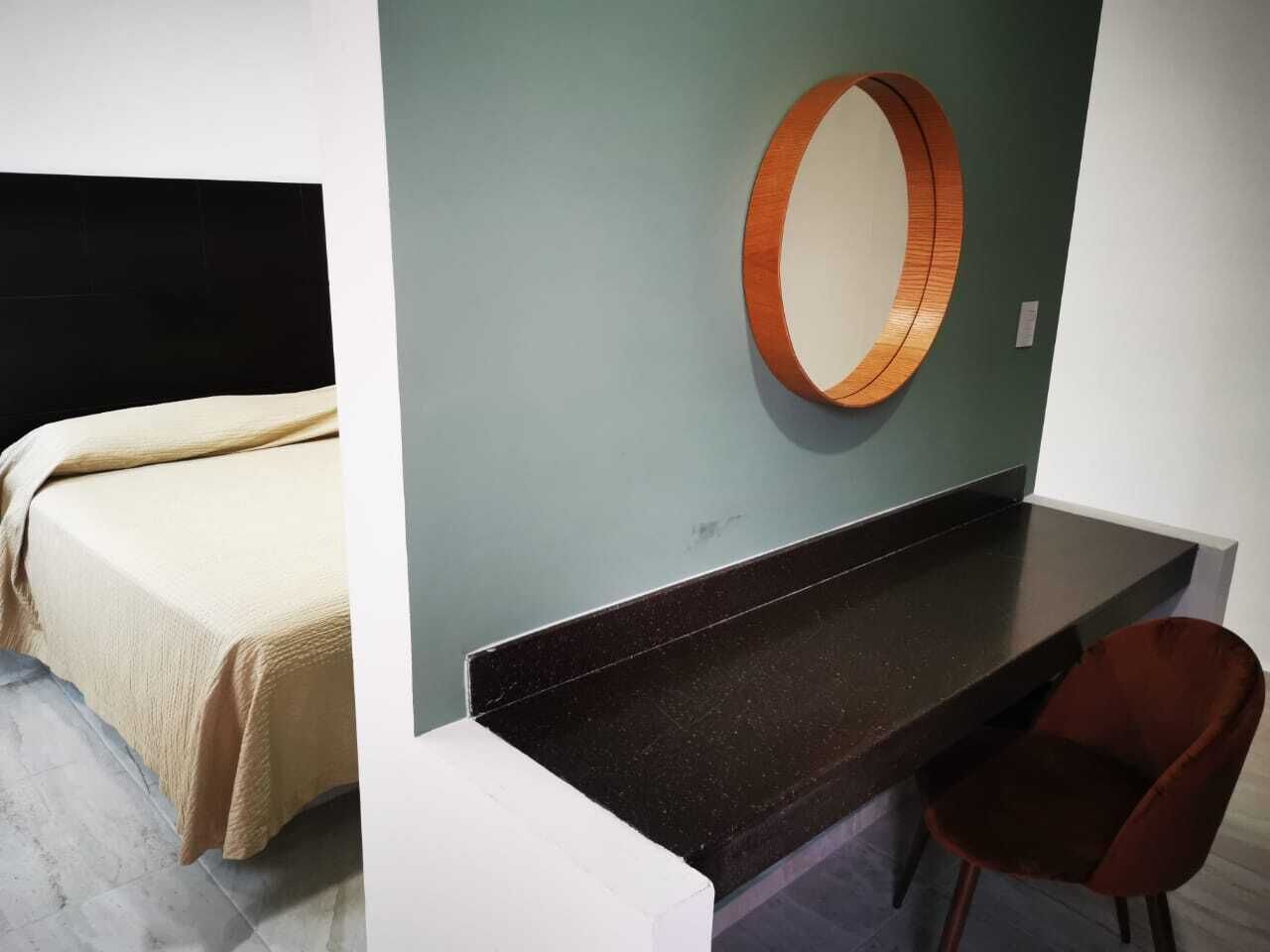 Una habitación con cama, escritorio, silla y un espejo colgado en la pared.
