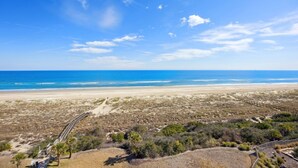 Una platja amb un passeig de fusta que condueix a l'oceà, envoltada d'una vegetació escassa.