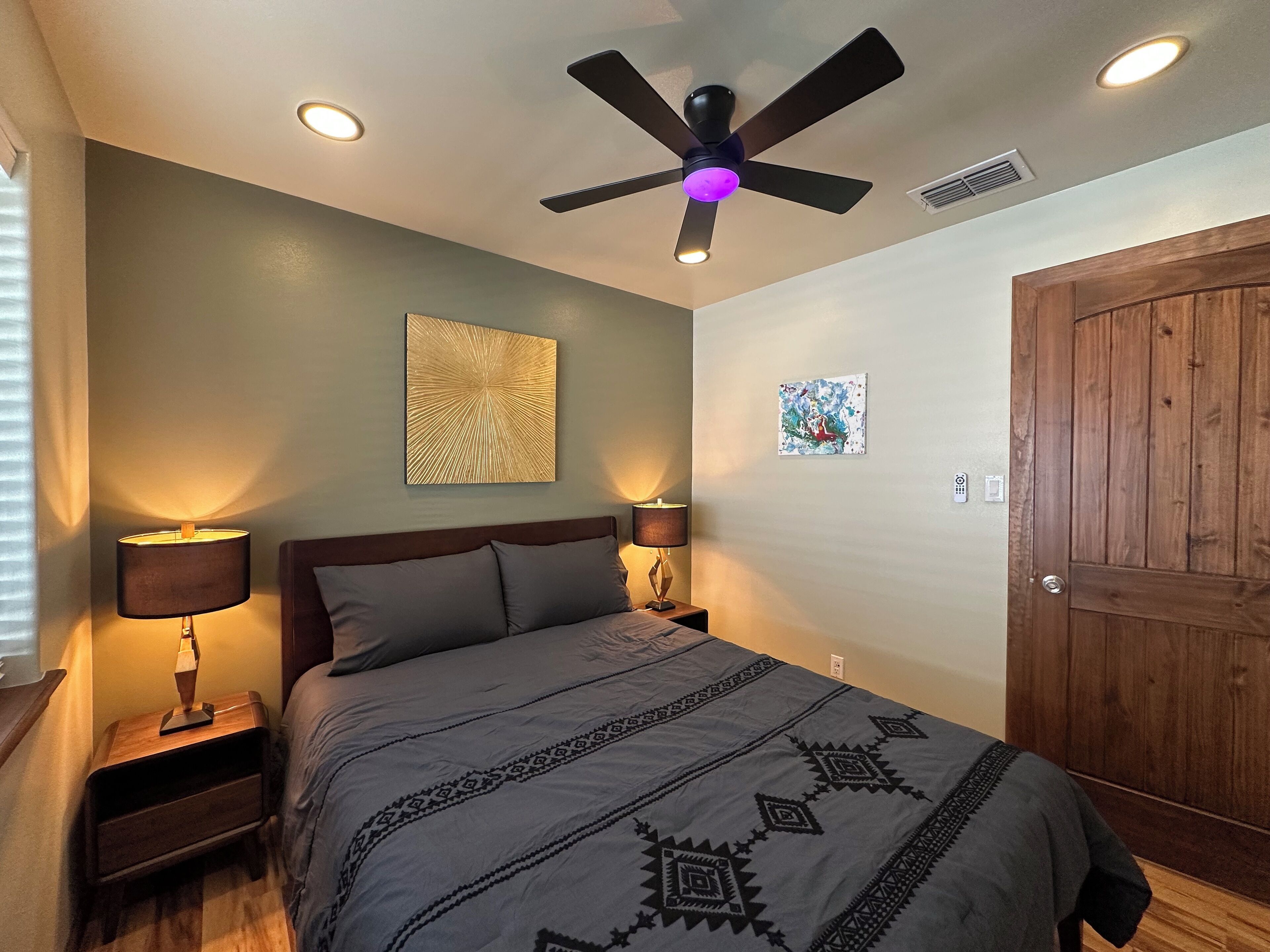 A bedroom with a bed, bedside lamps, a ceiling fan, and artwork on the walls.