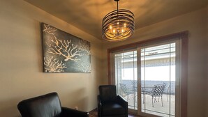 A room with a large sliding glass door leading to an outdoor patio, a black leather sofa, and a modern chandelier. - A&C WINDWARD COTTAGE # 2 (Victoria)
