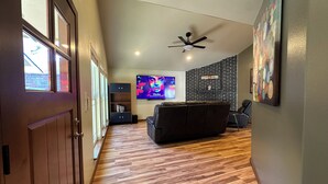 A hallway leading to a living area with a black leather sofa, a TV mounted on the wall, and a ceiling fan. - A&C WINDWARD COTTAGE # 2 (Victoria)
