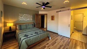A bedroom with a bed, a nightstand, a ceiling fan, and a wall-mounted artwork. - A&C WINDWARD COTTAGE # 2 (Victoria)