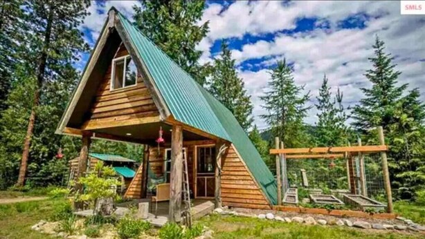 A wooden cabin with a sloped roof, a porch, and a fenced area with a ladder. - Pet friendly off grid chalet tucked away on a mountainside . (Sandpoint)