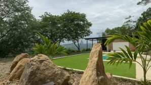 Un jardin aménagé avec de gros rochers, un petit bassin et un bâtiment en arrière-plan.
