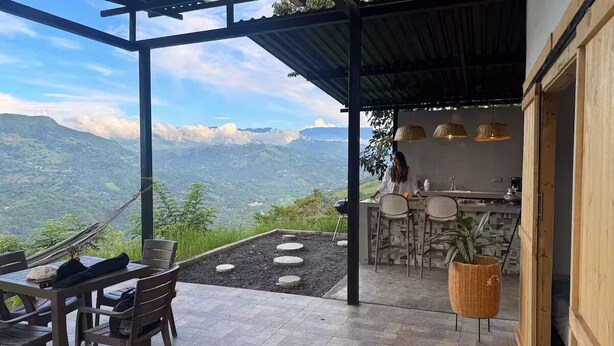 Une terrasse avec une table et des chaises pour les repas, un coin bar avec des tabourets et une vue sur les montagnes.