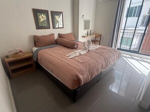 A neatly made bed with a pink bedspread and pillows, a bedside table with a lamp, and a window with a view of buildings. - Arch Club Patong (Patong)