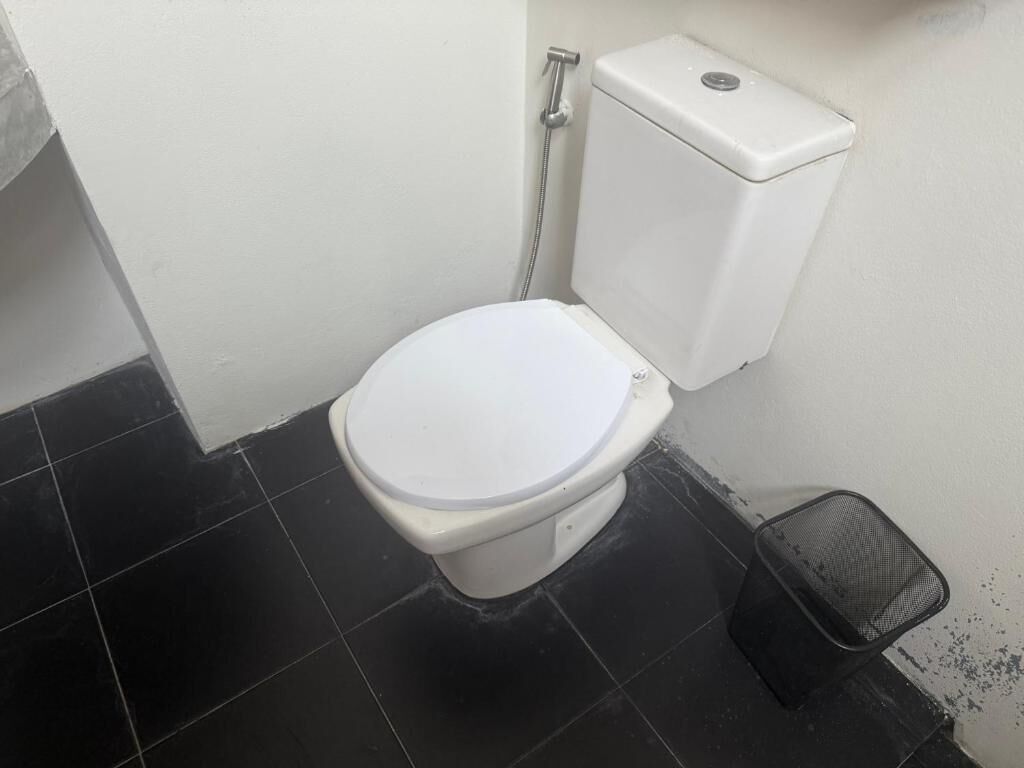 A small, compact bathroom with a white toilet, a black trash bin, and a white wall.