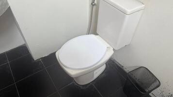 A small, compact bathroom with a white toilet, a black trash bin, and a white wall.