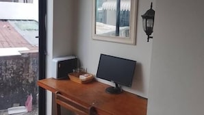 Pieni, moderni huone, jossa on puinen työpöytä, tietokone ja ikkuna, josta avautuu näkymä parvekkeelle.