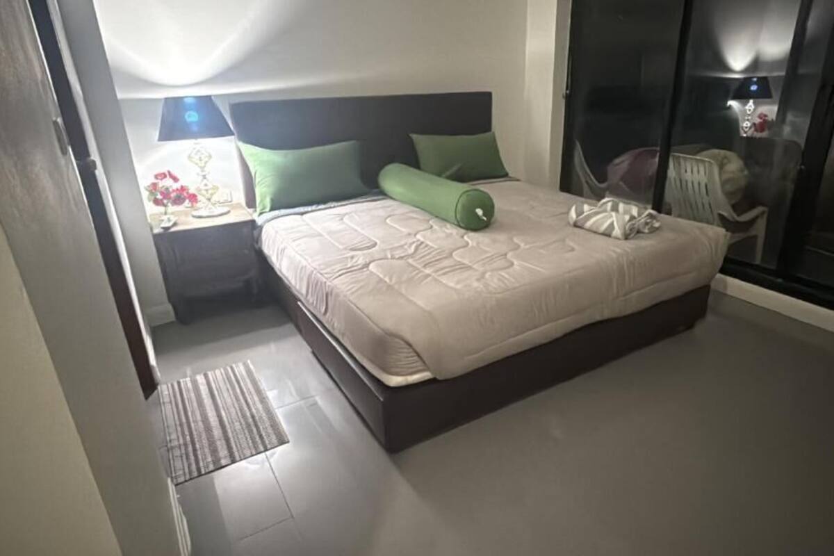A bedroom with a bed, a nightstand, a chair, and a large window.