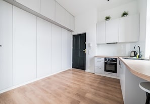 A modern kitchen with white cabinets, a black door, and a wooden countertop. - Kościuszki 73 City Center Studio (Poznań)