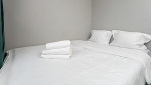 Un lit bien fait, avec du linge de lit blanc et des oreillers, un rideau vert sur la gauche et un mur sobre.