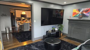 Ein modernes Wohnzimmer mit Fernseher, Kamin und einem durch einen offenen Durchgang einsehbarer Küche.