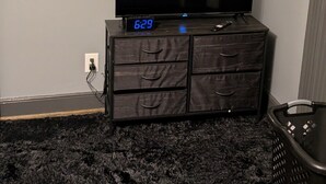 Ein Zimmer mit einem Flachbildfernseher auf einer Holzeinrichtung, einer Uhr, die 6:29 anzeigt, und einem Wandbild über dem Fernseher.