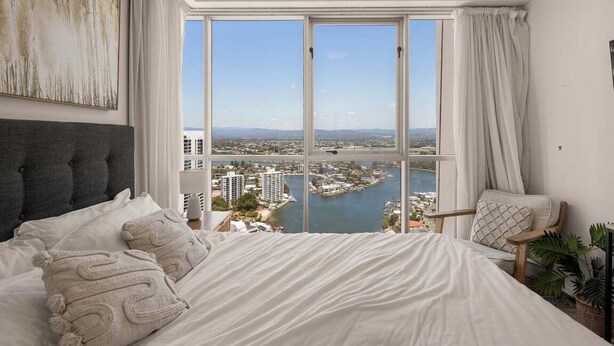 Ein Schlafzimmer mit einem großen Bett, Blick auf eine Stadt und Wasser, sowie einem Fenster mit Vorhängen.