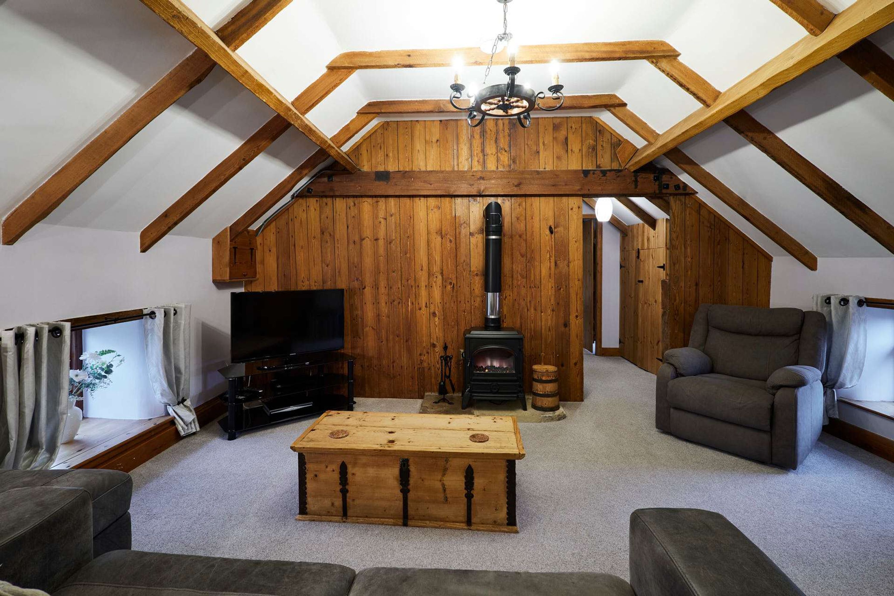 Ein gemütliches Wohnzimmer mit Holzbalkendecke, Kamin, Fernseher und bequemen Sitzgelegenheiten.