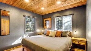 Un dormitorio con una cama grande, dos mesitas de noche y tres ventanas.