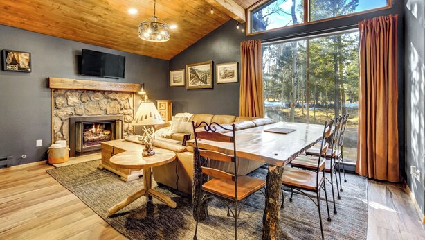 Un interior de cabaña acogedor con chimenea de piedra, una mesa de comedor grande y una zona de estar cómoda.