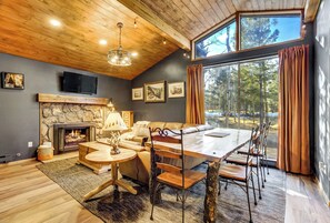 Un interior de cabaña acogedor con chimenea de piedra, una mesa de comedor grande y una zona de estar cómoda.