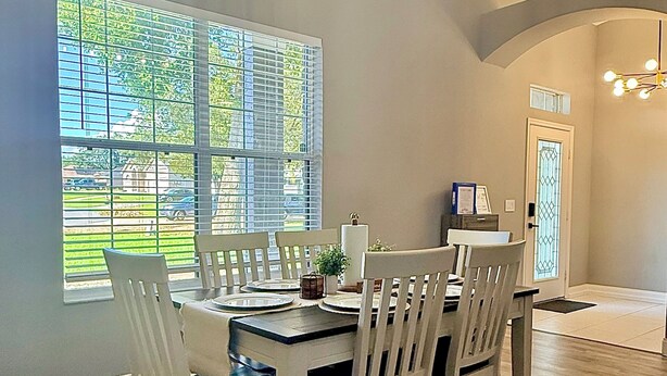 A dining area with a table set for four, white chairs, a chandelier, and a view through a window. - Rustic Modern Retreat w/ Private Pool – Leesburg (Leesburg)