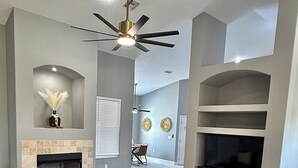 A spacious living room with a large L-shaped sectional sofa, a fireplace, a ceiling fan, and a flat-screen TV. - Rustic Modern Retreat w/ Private Pool – Leesburg (Leesburg)